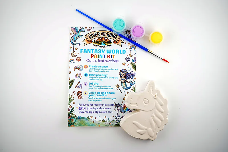 The Fantasy World kit as it ships: a plaster unicorn, three pots of paint and a brush, laid out with the printed instruction card.