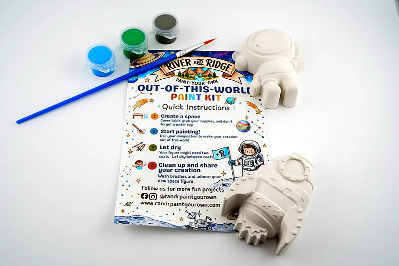 The Out-of-This-World kit as it ships: a plaster rocket and astronaut, three pots of paint and a brush, laid out with the printed instruction card.